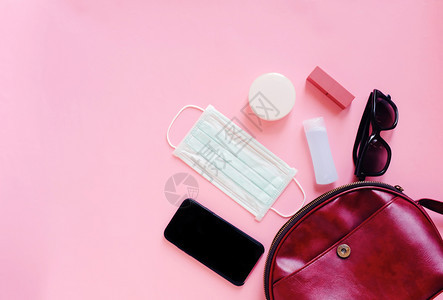 红皮女装袋打开有化妆品配件智能手机和面罩粉红背景上含酒精凝胶清洁剂复制空间防止可食19和冠状概念图片