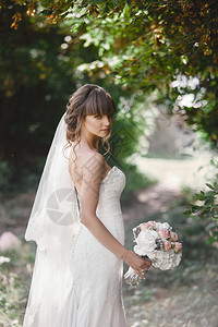 穿着优雅礼服的年轻新娘站在森林附近的田野上图片