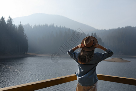 穿着帽子的快乐年轻女在山区享受湖边景色森林中放松的时刻尚女孩的背面景色享受户外清新自由人生活方式旅行和假期图片