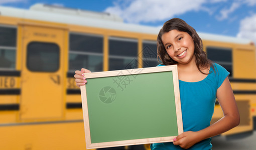 校车附近有空白黑板的年轻女西班牙学生图片