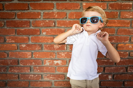可爱的男孩戴着墨镜站在砖墙上背景图片