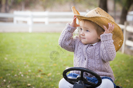 戴着牛仔帽的女孩开心的坐在玩具拖拉机上图片