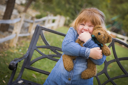 可爱的笑年轻女孩拥抱她的泰迪熊在板凳外面图片