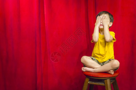 混血男孩在红幕前坐凳子上遮着眼睛图片