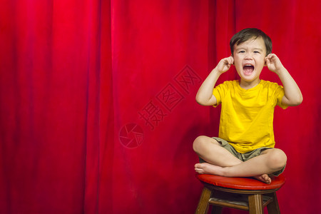 混血男孩他耳朵里有手指坐在红幕前的凳子上高清图片