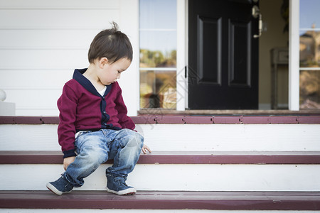 坐在前门廊台阶上的可爱忧郁混血男孩图片