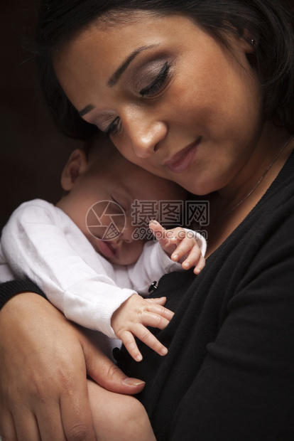 年轻有吸引力的少数民族妇女将新生婴儿放在引人注目的照明下图片