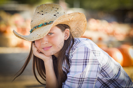穿着牛仔帽肖像的未成年少女穿着牛仔帽在南瓜草地一个生锈的设置图片