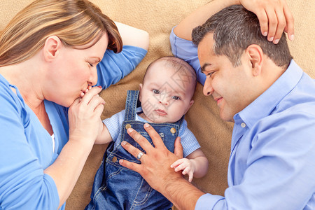 年轻夫妇带婴儿躺在地毯上母亲亲吻着婴儿的手图片