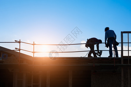 夕阳下建筑工人在屋顶上的背景图片