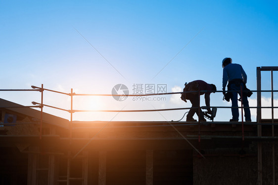 夕阳下建筑工人在屋顶上的背景图片