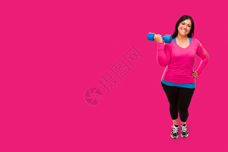 穿着运动服的中年女拿着哑铃面对明亮的紫红色粉背景图片