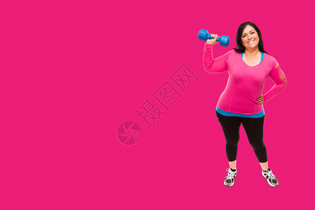 穿着运动服的中年女拿着哑铃面对明亮的紫红色粉背景图片