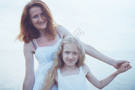 母亲和女儿穿着白裙子走在海边图片
