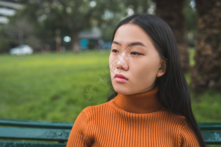 坐在公园户外的长椅上年轻美丽的亚洲女人肖像图片