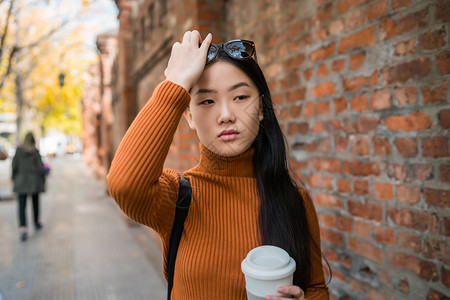 年轻亚洲女在街上露天站着时拿咖啡杯图片