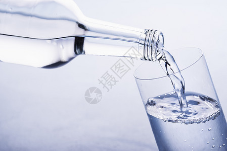 将水从玻璃瓶倒到蓝色背景的玻璃杯图片