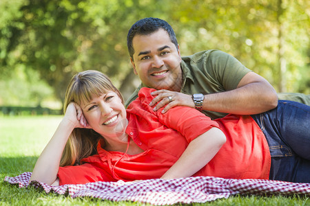 快乐的有吸引力混合种族夫妇肖像在公园的毯子上图片