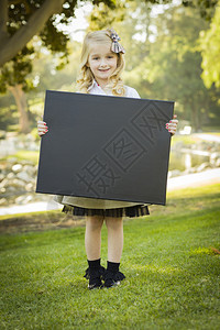 可爱的金发小姑娘头上有个弓在户外拿着黑的白板图片