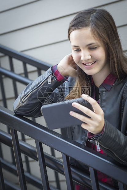 坐在楼梯上微笑的年轻女孩看着智能手机图片