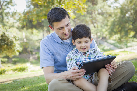 父亲和儿子在户外草坪上玩平板电脑图片