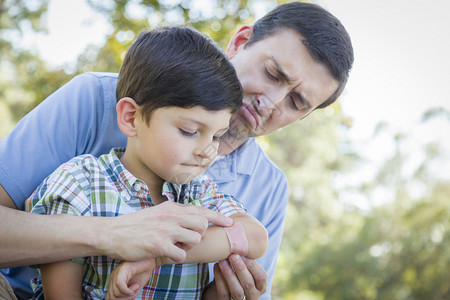 慈爱的父亲给他在公园的年轻儿子肘部绑上绷带图片