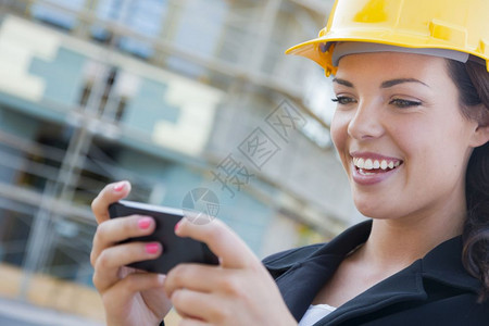 年轻女专业承包商在对接站点上戴着硬帽用手机发短信图片
