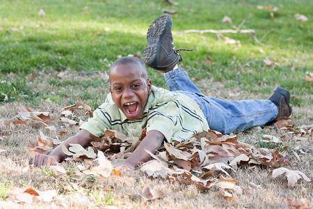 英俊的非裔美国男孩在公园里玩耍树叶之间图片