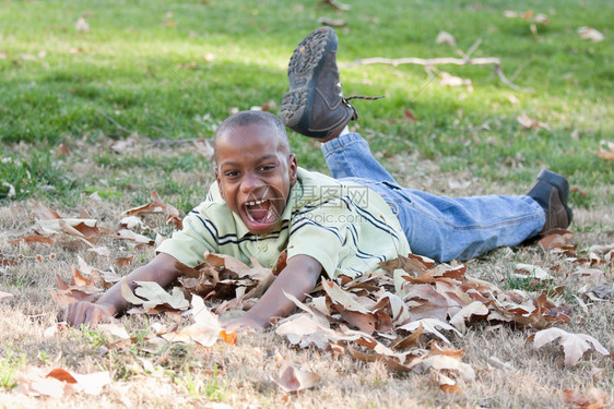 英俊的非裔美国男孩在公园里玩耍树叶之间图片