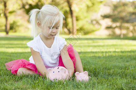 可爱的小女孩玩得开心与她的大和小猪银行外面的草地上图片