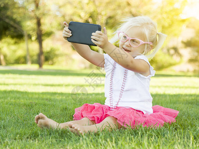 坐在草地上的可爱小女孩用手机拍自图片