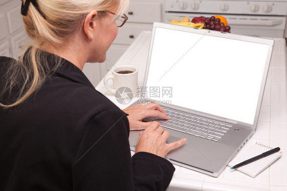 妇女坐在厨房里用带空白屏幕的笔记本电脑屏幕可以很容易地用于使包含剪切路径的自己信息或图片图片