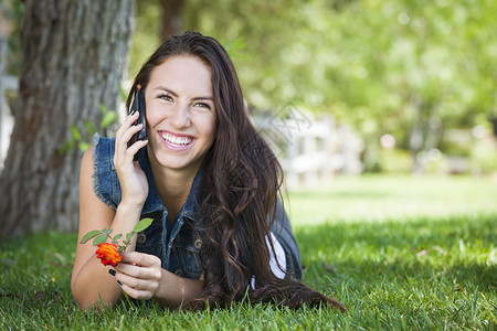 快乐的混合种族年轻女在外面用手机聊天躺在草地上图片