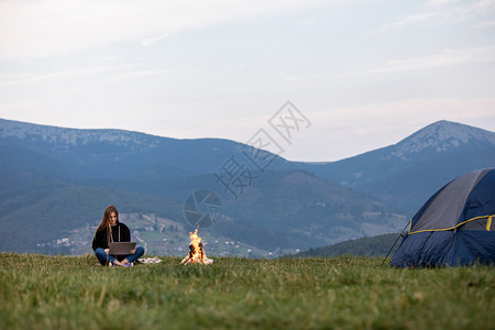 青年女自由职业者晚上在山区用笔记本电脑工作游客女孩坐在营火附近玩得开心复制空间年轻女自由职业者晚上在山区用笔记本电脑工作旅游女孩图片