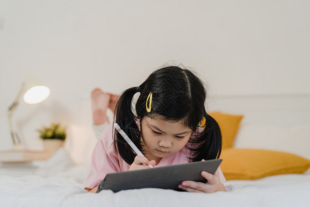 小女孩趴在床上写作业图片素材