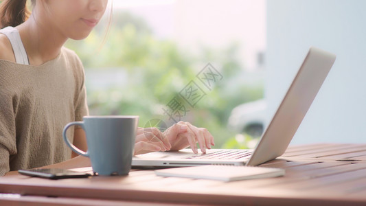在家工作的女自由职业者早上在花园的桌用笔记本电脑工作的女商人在家里工作的妇女生活方式概念图片