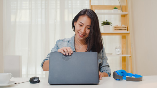 在家客厅工作时使用笔记本电脑穿衣快乐的年青轻女孩放松坐在书桌上寻找工作在互联网上做工作图片