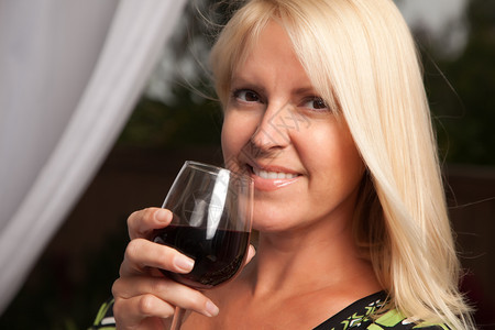 美丽的金发女微笑的人在一个晚上的社交聚会品尝葡萄酒图片