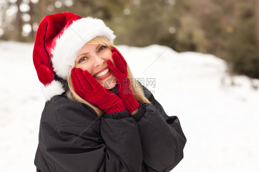 穿着金发女人的漂亮圣诞帽冬天在雪上玩得开心图片