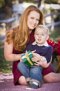 英俊的年轻男孩拿着圣诞礼物和他妈在公园里图片