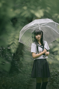 下雨时在自然行走道上带着雨伞行走的亚裔女学生肖像图片