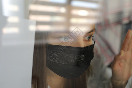 在家中玻璃窗后戴医疗面具的年轻女冠状流行的隔离概念有19个选择焦点图片