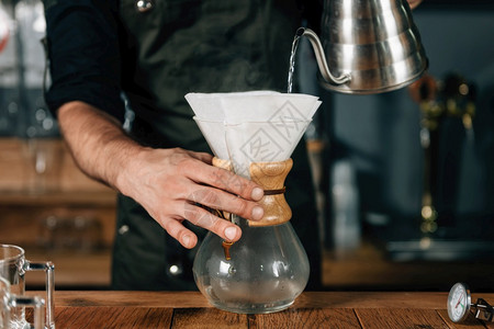 咖啡厅将水从壶倒入白色过滤器用于咖啡身穿黑制服的纹手臂咖啡师图片