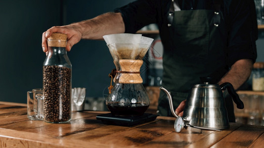 贴上过滤咖啡机温度计水壶和木制桌子上的数字尺度身穿黑色制服的纹身手臂咖啡师图片