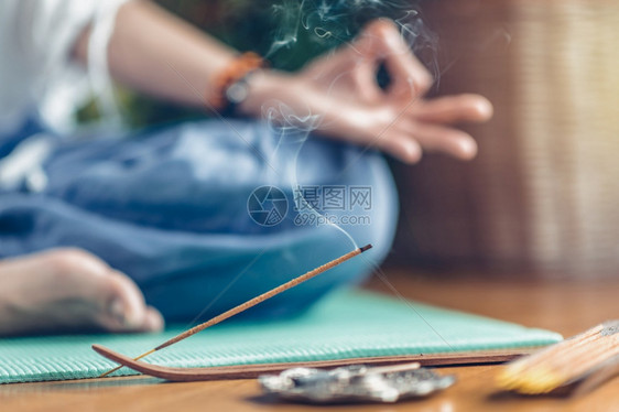 在木地板的绿瑜伽垫上沉睡的女人专注于香棍和烟雾在背景中无法认出的瑜伽练习者训练后放松图片