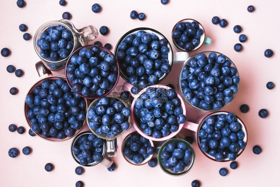 带有机蓝莓不同大小的杯子高于视图粉红色桌上的杯子中含有蓝莓水果粉红色背景的新鲜蓝莓顶层视图图片