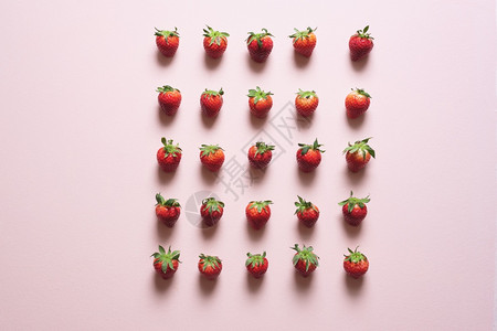有机草莓水果排列在行内各间距离相等粉红色桌子上的新鲜草莓在上视图中图片