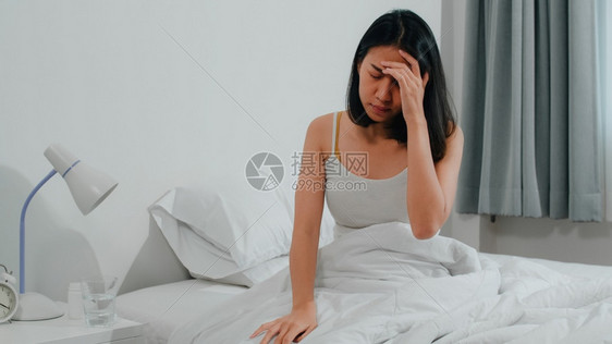 患有不健康疾病的印度裔女患有失眠症身为一名年轻女上午在家卧室的床上吃止痛药以减轻头和喝杯水图片