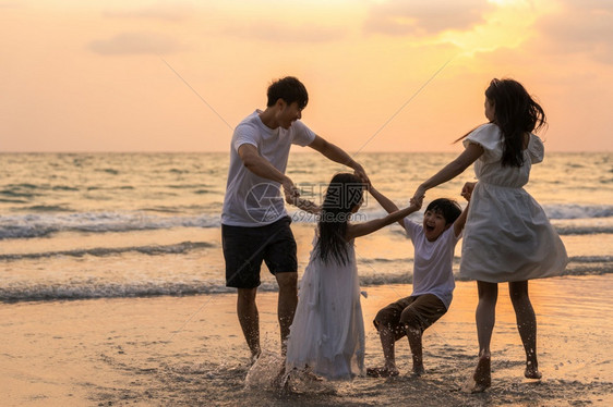 父亲妈和孩子在太阳落日时放松在海上玩耍生活方式是渡假暑概念图片