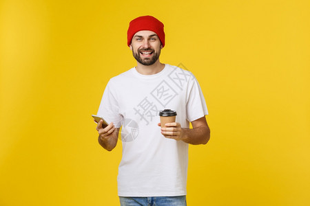 一位穿着便衣的快乐青年男子肖像身着便衣站在黄色背景之外拿着手机喝咖啡图片